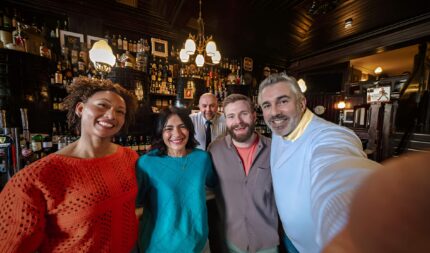 Group enjoying drinks at a cosy pub in Harveys Guesthouse, smiling warmly at the camera.