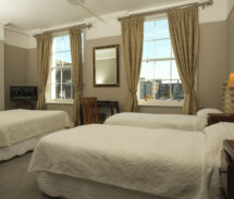 Cosy guesthouse room with twin beds, soft lighting, and a city view through large windows.