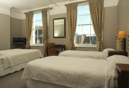 Cosy guesthouse room with twin beds, soft lighting, and a city view through large windows.