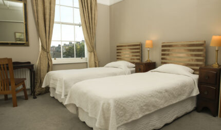 Cosy guestroom with twin beds, elegant decor, warm lighting, and a large window view.