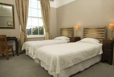 Cosy guestroom with twin beds, elegant decor, warm lighting, and a large window view.