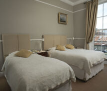 Cosy guest room with twin beds, warm decor, large window overlooking city, ideal for families.