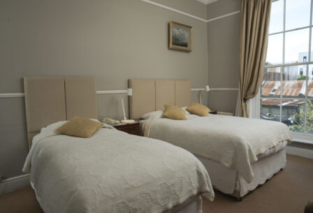 Cosy guest room with twin beds, warm decor, large window overlooking city, ideal for families.
