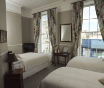 Cosy guest room with floral curtains, twin beds, and street view windows.