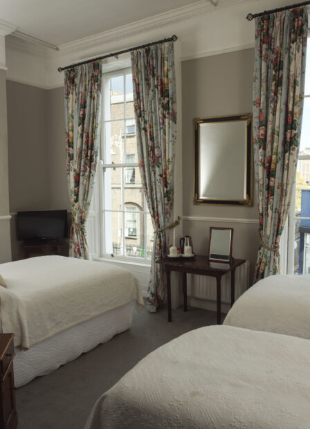 Cosy guest room with floral curtains, twin beds, and street view windows.