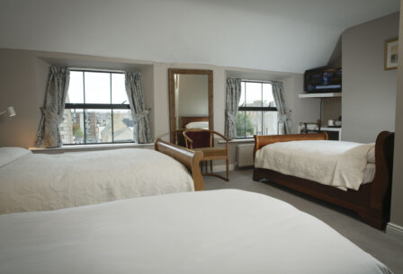 Cosy guesthouse room with two beds, large windows, and a TV; perfect for families.