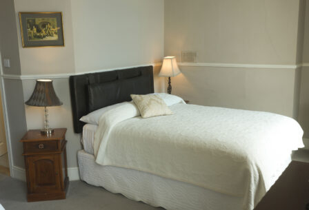 Cosy double bed in a warmly lit Harveys Guesthouse room, with elegant lamps and a classic painting.