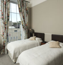 Cosy guesthouse room with twin beds, floral curtains, and large window view.
