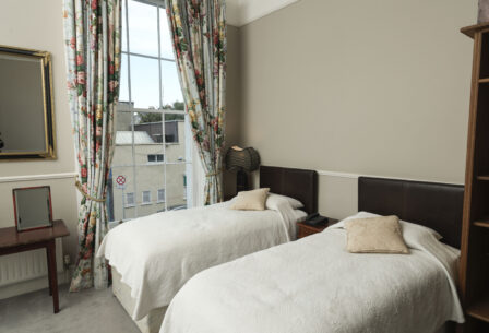Cosy guesthouse room with twin beds, floral curtains, and large window view.