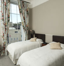 Cosy guestroom with twin beds, floral curtains, and a bright window view at Harveys Guesthouse.