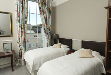 Cosy guestroom with twin beds, floral curtains, and a bright window view at Harveys Guesthouse.