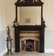 Elegant wooden fireplace with ornate mirror in cosy guesthouse room.