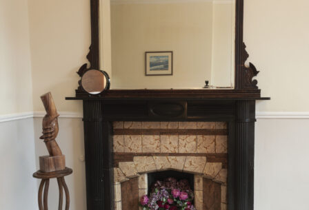 Elegant wooden fireplace with ornate mirror in cosy guesthouse room.