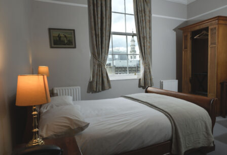 Cozy guesthouse room with a soft-lit lamp, comfy bed, and a view of a charming cityscape.