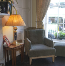 Cosy guest lounge with armchair, lamp, and garden view at Harveys Guesthouse.