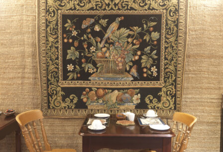 Cosy dining nook with ornate tapestry and wooden chairs.
