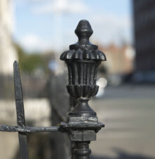 Elegant black iron fence outside Harveys Guesthouse, with a blurred city street in the background.