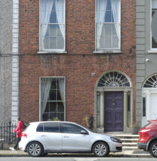 Charming brick guesthouse facade with purple door, touched by sunlight.