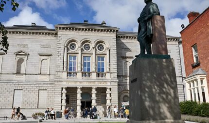 Guests enjoy sunny day outside Harveys Guesthouse, with historic architecture and vibrant atmosphere.