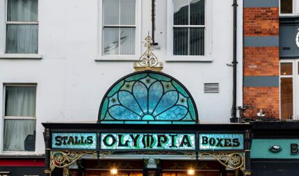 Group walking past a historic theatre entrance on a lively street.