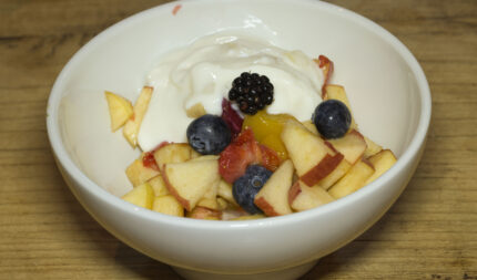 Fresh fruit salad with yoghurt in a white bowl on a wooden table, offering a healthy breakfast option at Harveys Guesthouse.