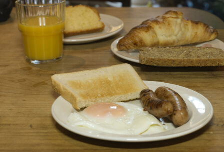 Hearty breakfast with eggs, sausages, toast, croissant, and orange juice on wooden table.