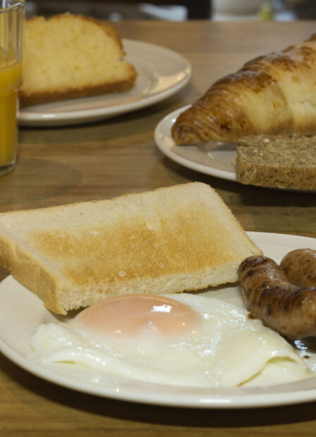 Hearty breakfast with eggs, sausages, toast, croissant, and orange juice on wooden table.