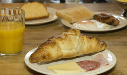 A hearty breakfast spread featuring a croissant, cold cuts, cheese, and a refreshing glass of orange juice awaits guests at Harveys Guesthouse.