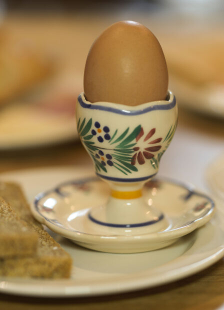 Cosy breakfast with egg in decorative cup, fresh bread, and orange juice on a wooden table.